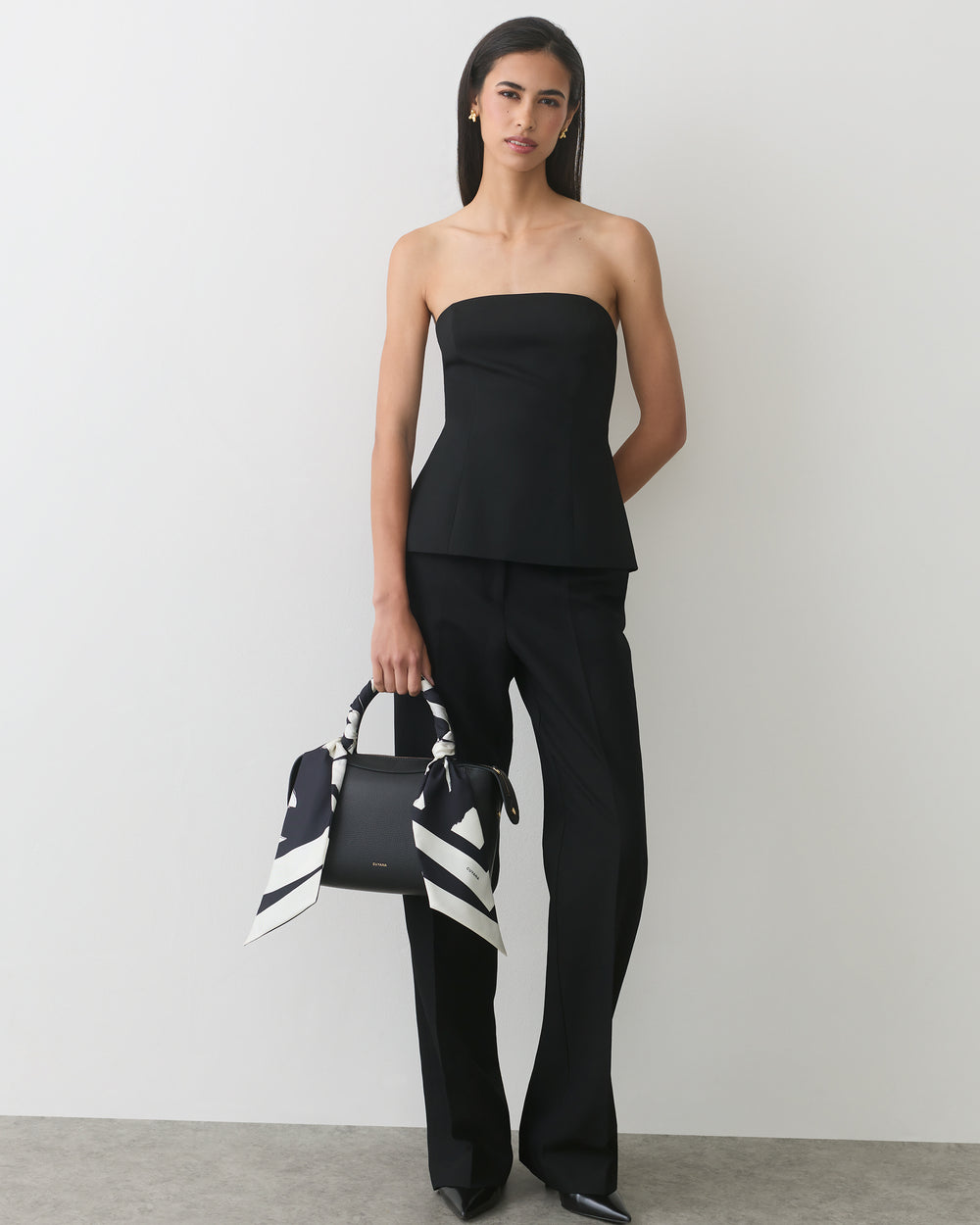 Person in strapless top and pants holding handbag with patterned scarf.