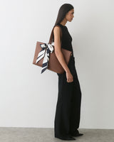 Person in sleeveless outfit carrying a bag with a tied scarf.