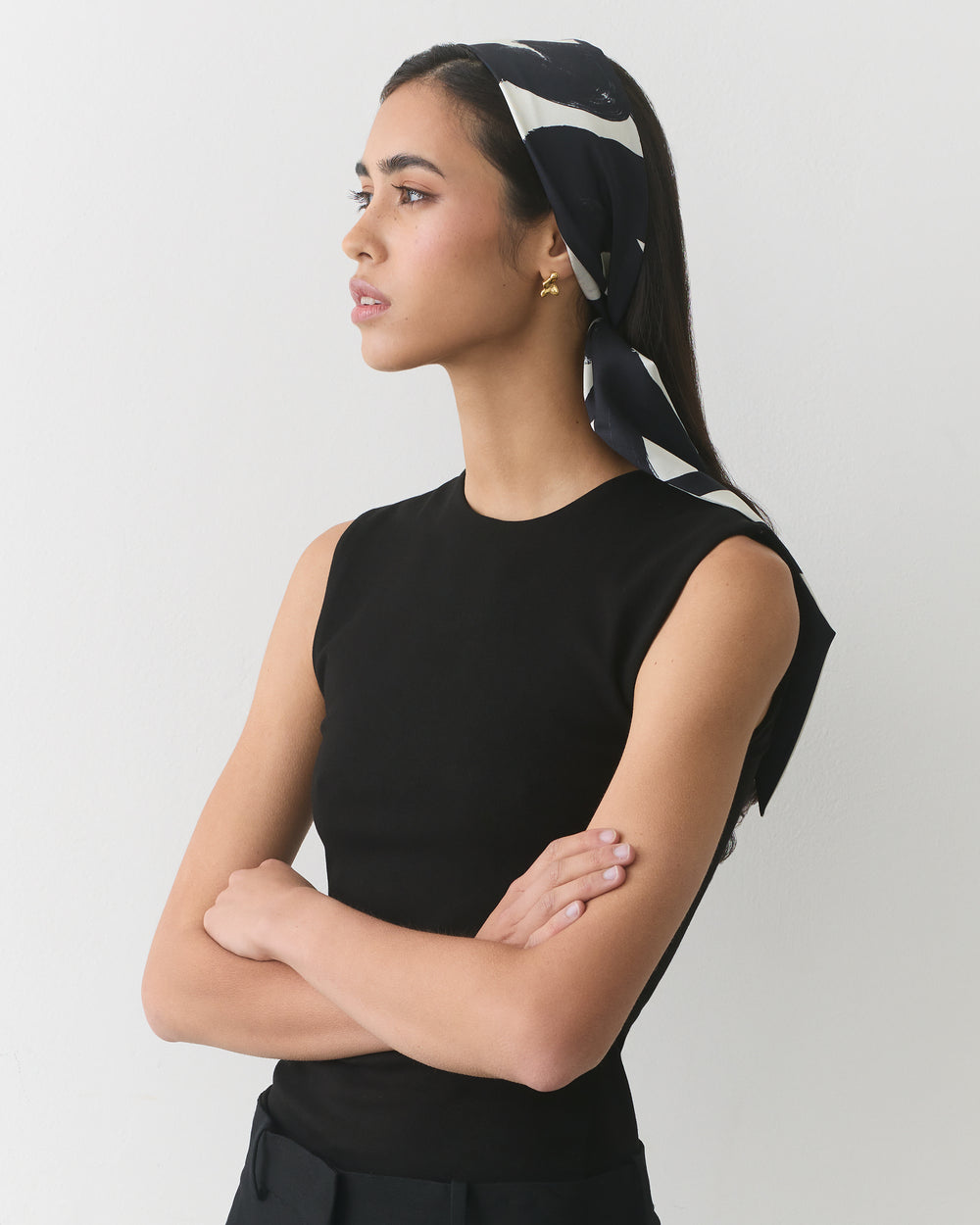 Person wearing a sleeveless top and headscarf, standing with arms crossed.