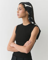 Person wearing a sleeveless top and headscarf, standing with arms crossed.