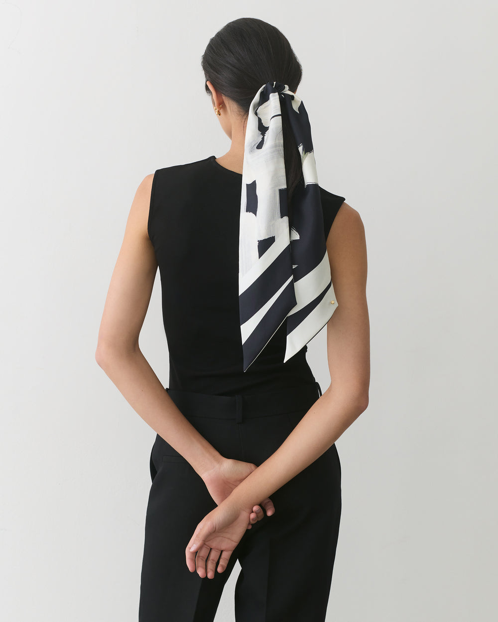 Person facing away with scarf tied around ponytail, arms behind back.