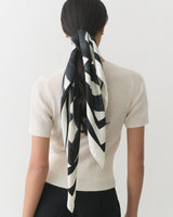 Person with scarf tied around ponytail, wearing short-sleeve top.