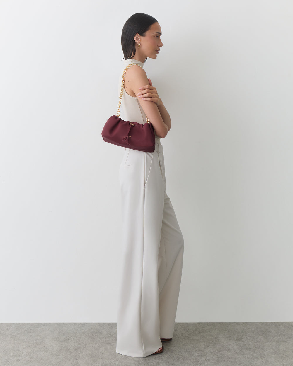 Person holding a small purse with a chain strap, wearing sleeveless top and wide-leg pants.