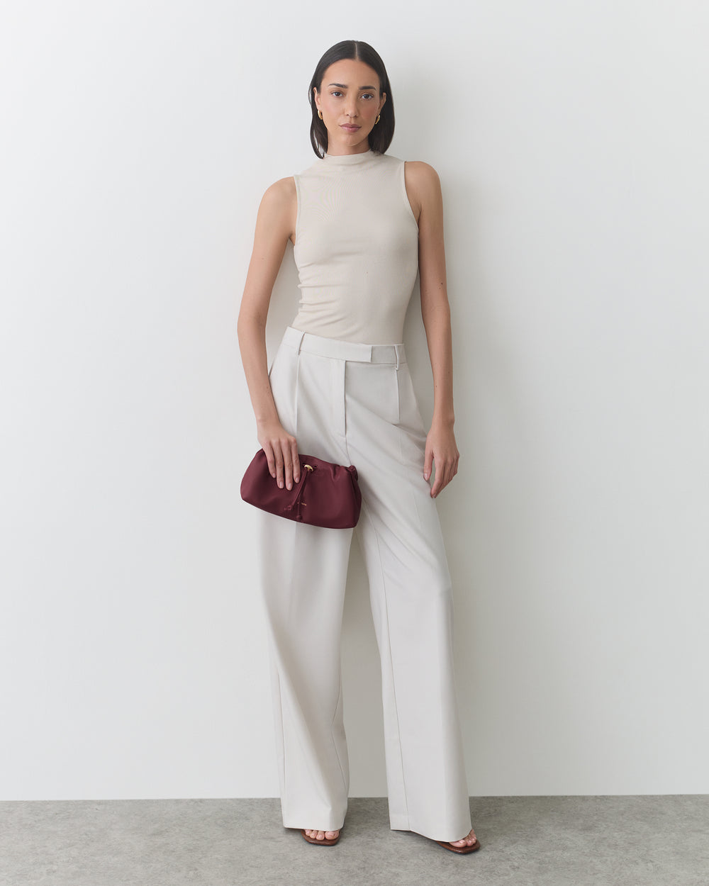 Person in sleeveless top and wide-leg pants holding a clutch.