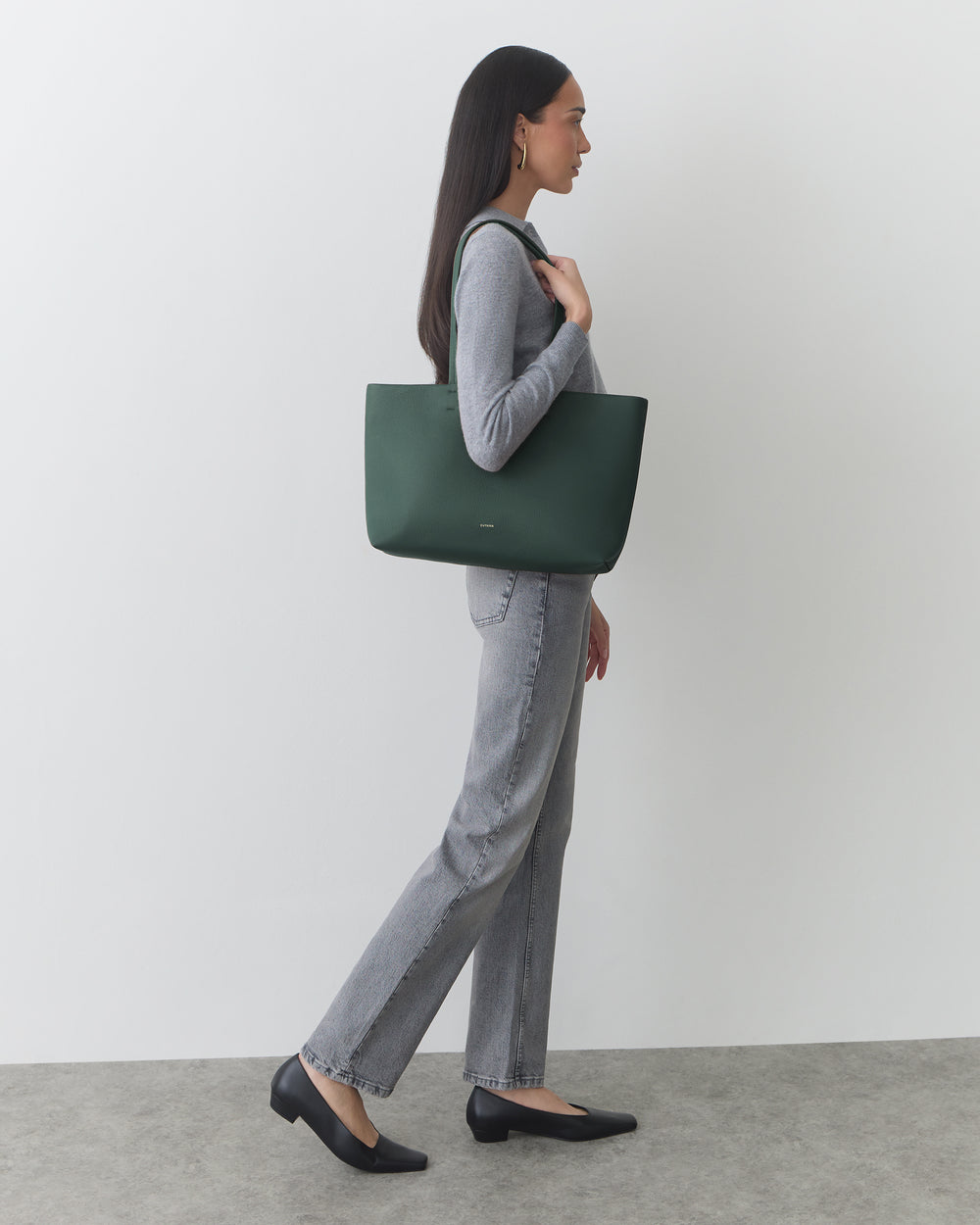 Person standing, holding a large tote bag over shoulder, wearing casual clothing and shoes.