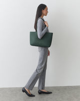 Person standing, holding a large tote bag over shoulder, wearing casual clothing and shoes.