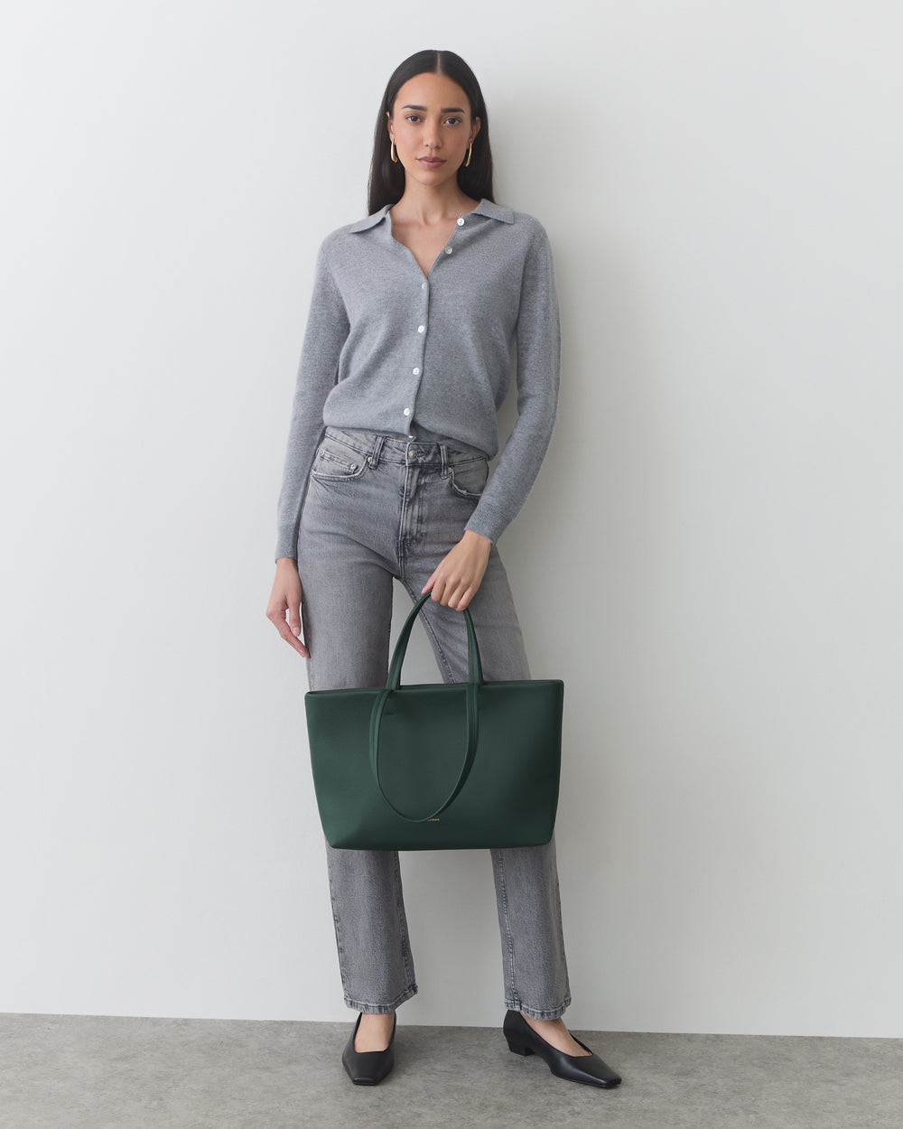 Person standing against a wall holding a large tote bag.