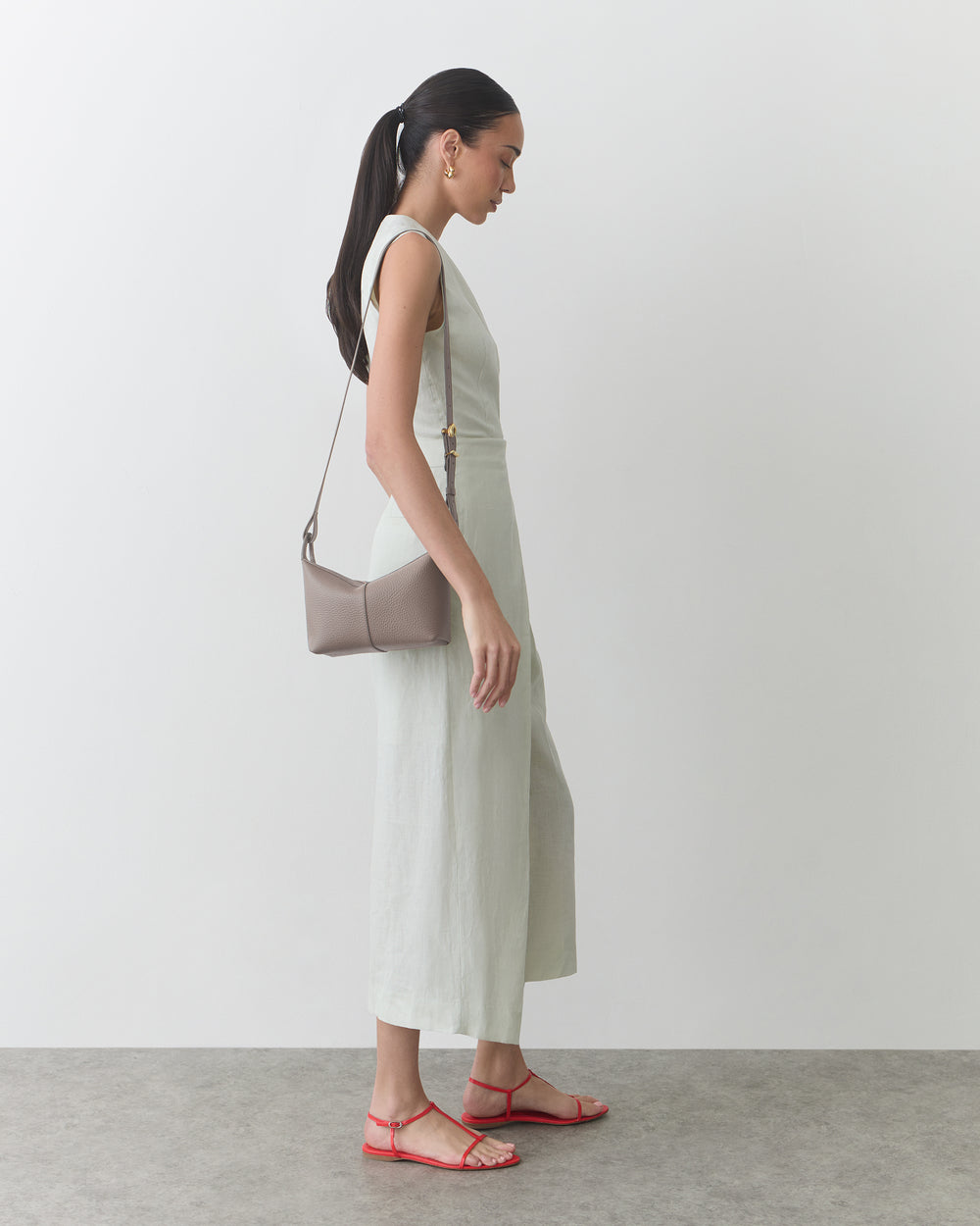 Person wearing sleeveless dress with shoulder bag and sandals standing on concrete floor