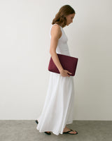 Woman in long dress holding a rectangular clutch under her arm, standing indoors.