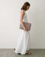 Person in dress holding a large clutch bag, wearing sandals, standing indoors.