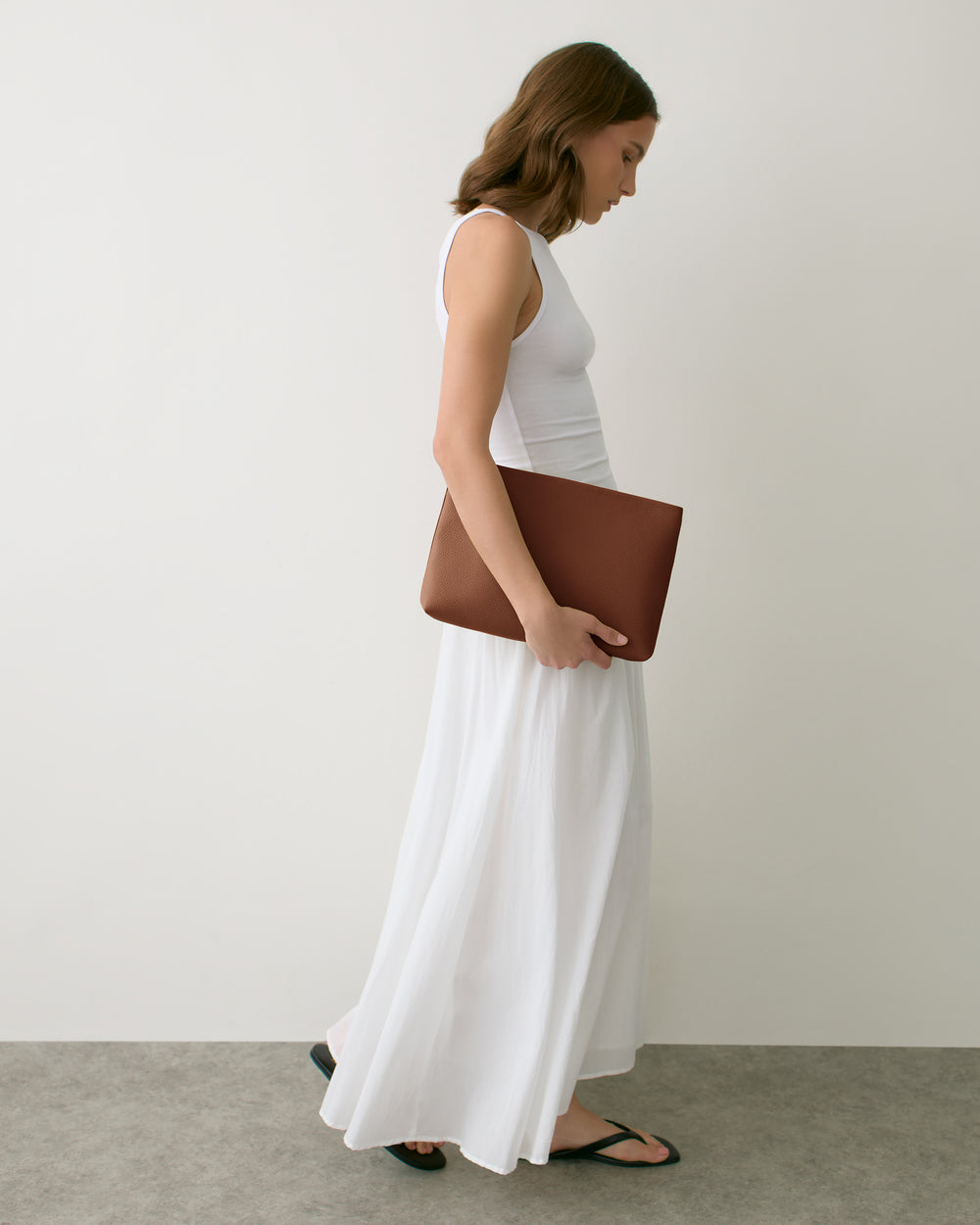 Person in a long dress holding a large clutch, walking indoors.