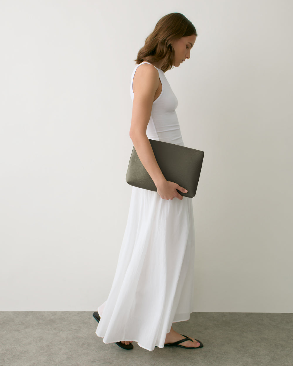 Person walking holding a large envelope pouch, wearing a long dress and sandals.
