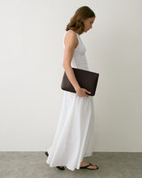 Person in long dress holding a portfolio, walking in side profile.