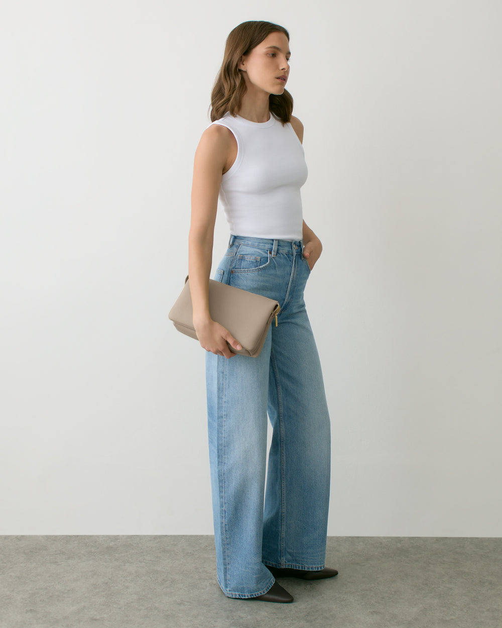 Person in sleeveless top and jeans holding a clutch bag.