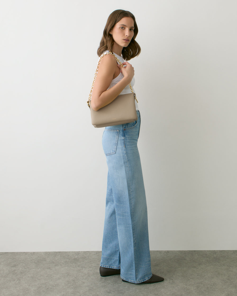 Person in jeans holding a shoulder bag, standing against a plain background.