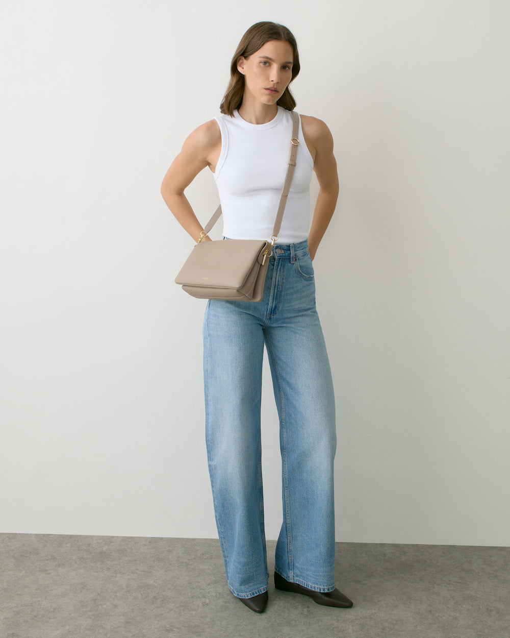 Person wearing sleeveless top, wide-leg jeans, and crossbody bag.