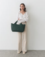 Person standing with a travel bag, wearing long-sleeve top and wide-leg pants.