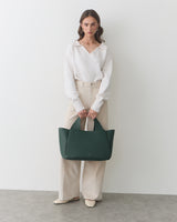 Person holding a large handbag, standing against a plain background.