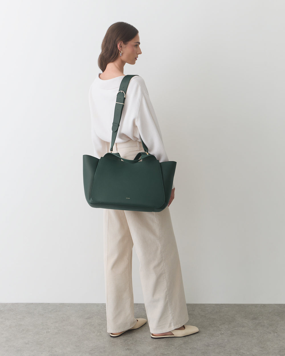 Person standing holding a travel bag over shoulder.