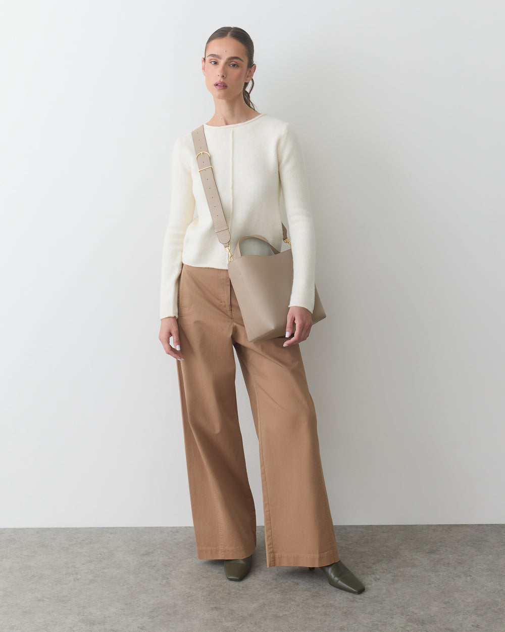 Person wearing a sweater and wide-leg pants, holding a shoulder bag.