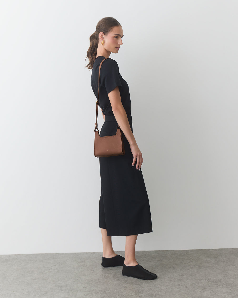Model standing sideways with crossbody bag wearing a dress and slip-on shoes