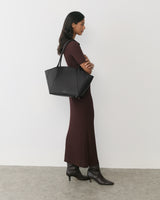 Person in long dress holding a large bag, wearing ankle boots, standing on concrete floor.