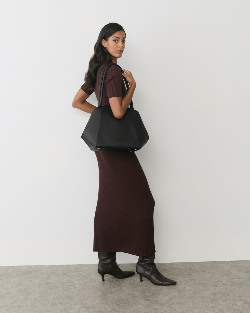 Person in long dress holding a large shoulder bag. 