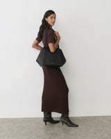 Person in long dress holding a large shoulder bag. 