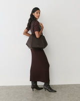 Person in long dress holding large handbag, standing on gray floor.