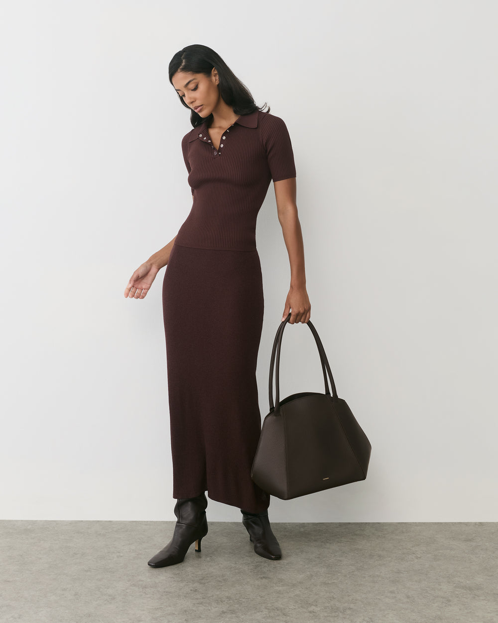 Person in long dress, holding a shoulder bag by its handle. 