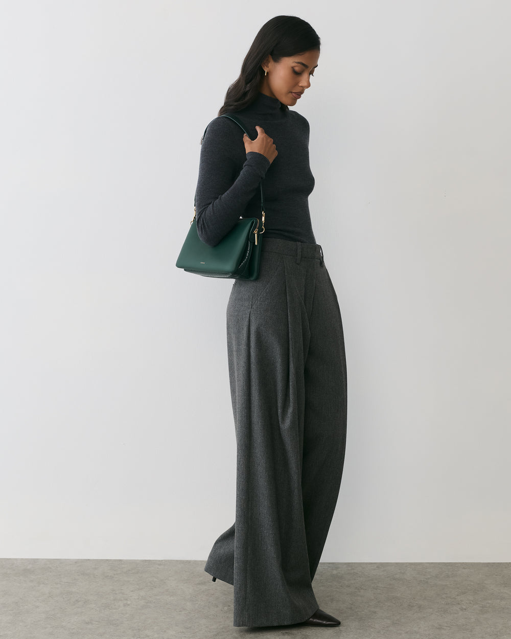 Person in a turtleneck and wide-leg pants holding a shoulder bag.