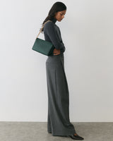 Person in a long-sleeve top and wide-leg pants, holding a shoulder bag.