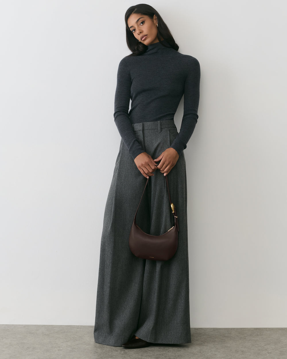 Person in turtleneck and wide-leg pants holding shoulder bag.