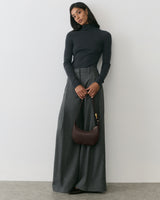 Person in turtleneck and wide-leg pants holding shoulder bag.
