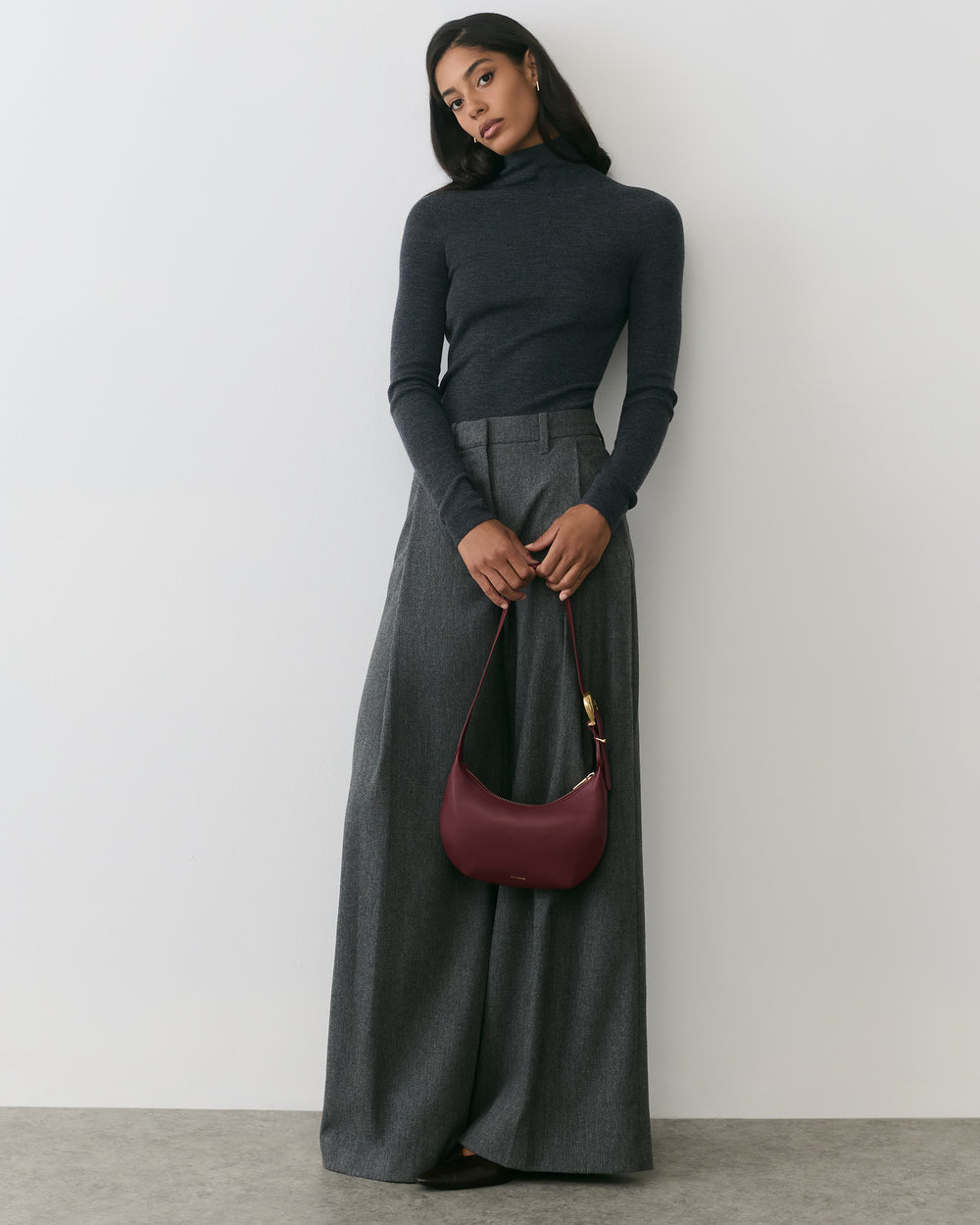 Person in turtleneck and wide-leg pants holding a bag.
