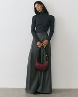 Person in turtleneck and wide-leg pants holding a bag.