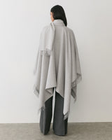 Person wearing a long cape standing with back to the camera.