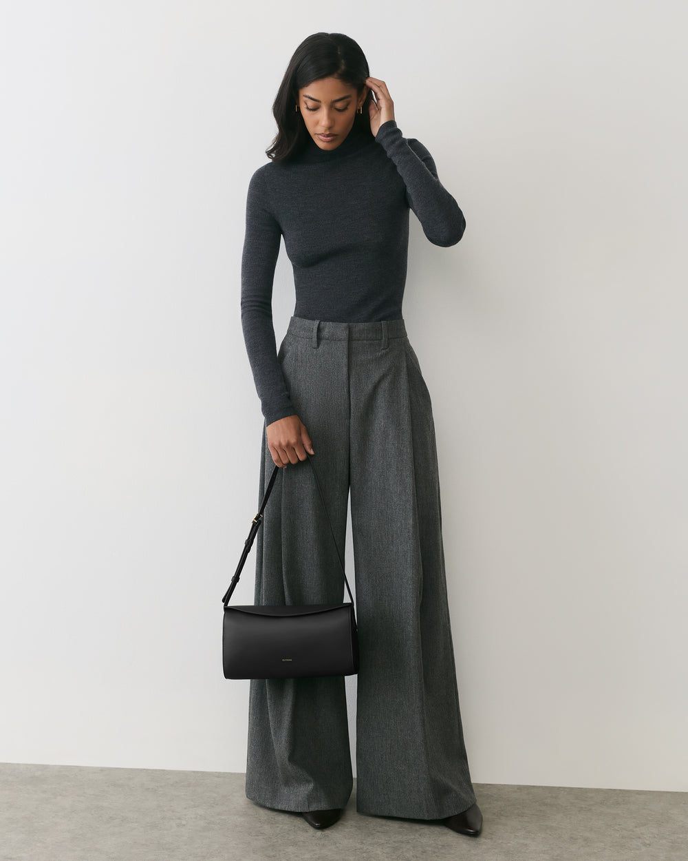 Person in long-sleeve top and wide-leg pants holds a shoulder bag