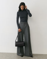Person in long-sleeve top and wide-leg pants holds a shoulder bag