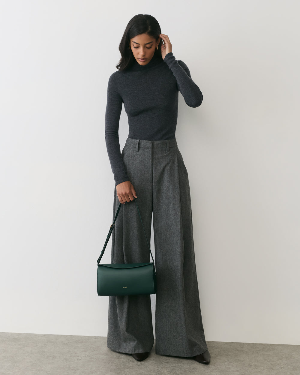 Person wearing a long-sleeve top and wide-leg pants, holding a shoulder bag.