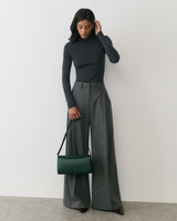 Person wearing a long-sleeve top and wide-leg pants, holding a shoulder bag.