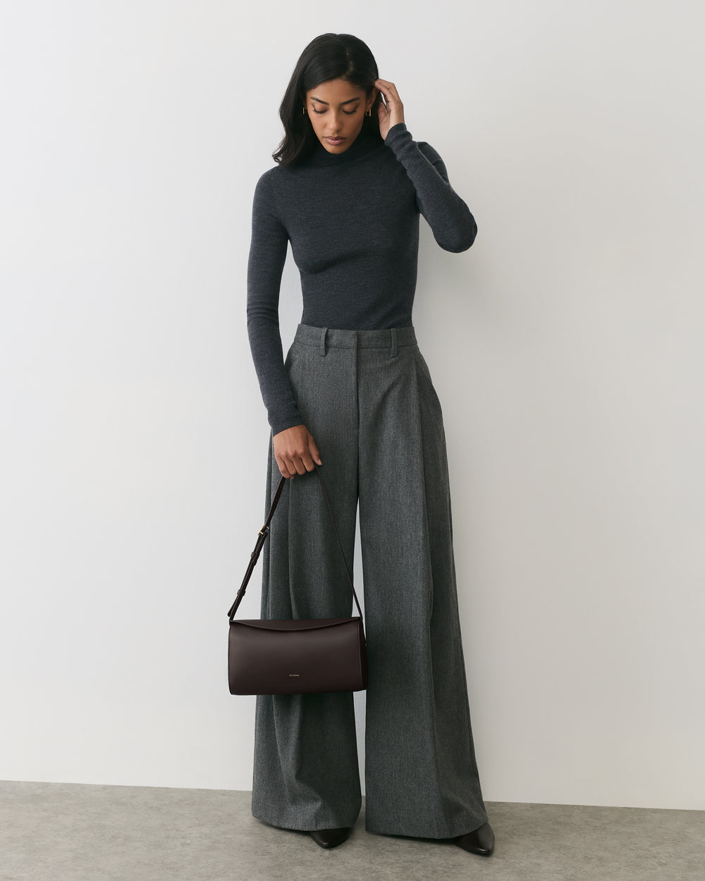 Woman in long-sleeve top with wide-leg pants holding a handbag.