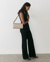 Person standing with a purse over shoulder, wearing a sleeveless top and wide-legged pants.