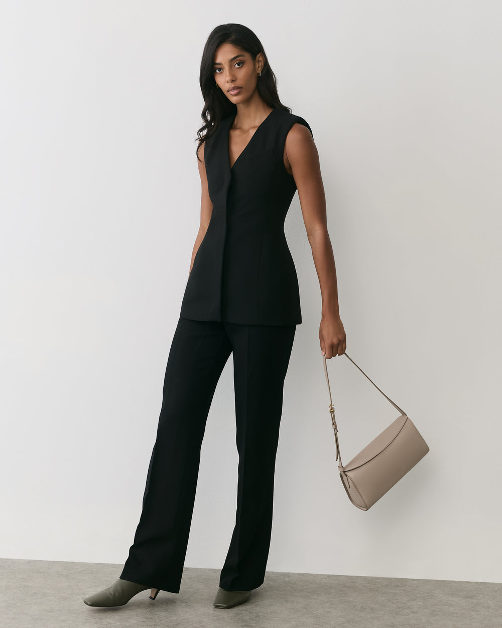 Woman in a sleeveless suit holding a shoulder bag.