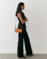 Person stands wearing a sleeveless outfit with a shoulder bag.