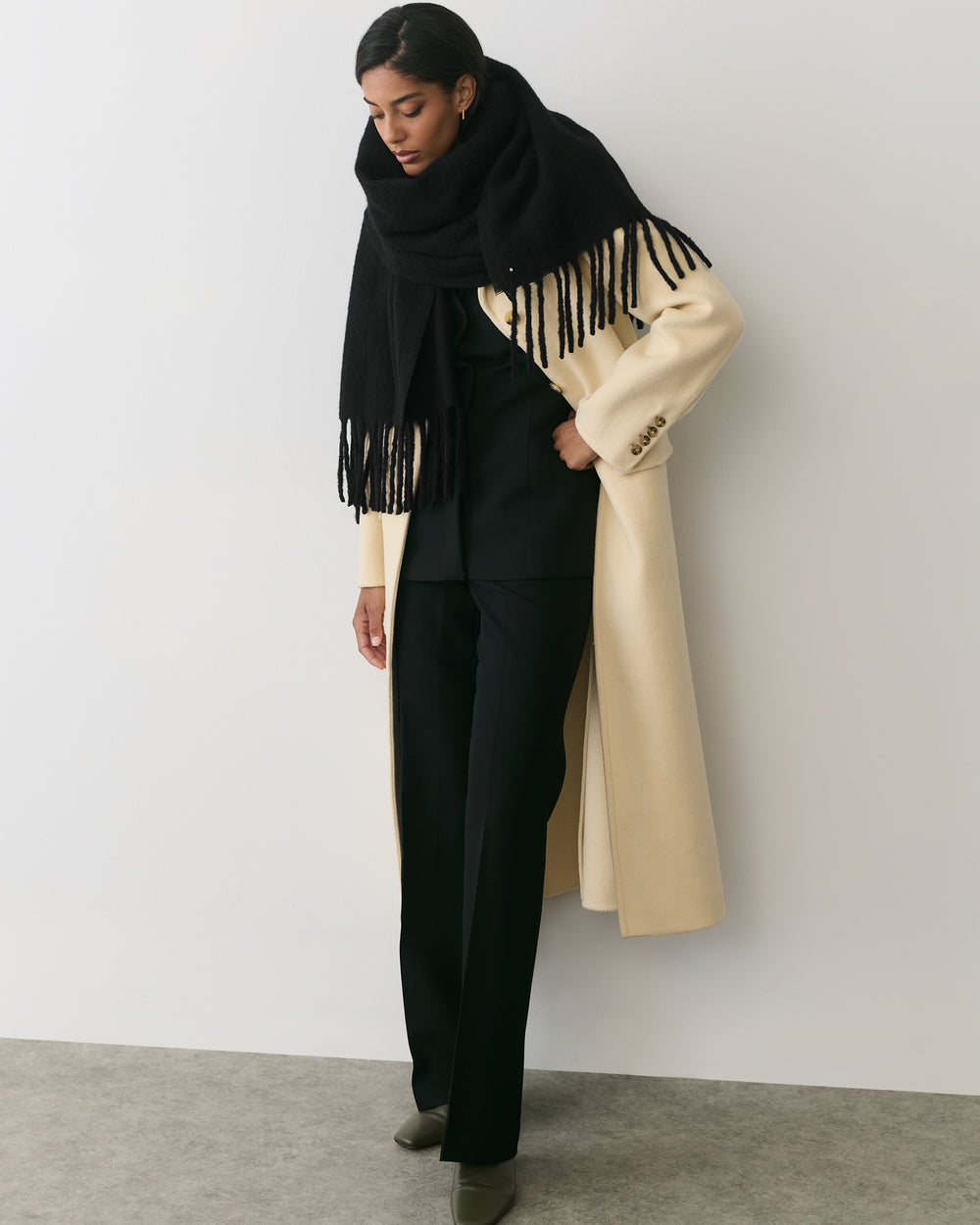 Person in a long coat with a fringed scarf looking down.