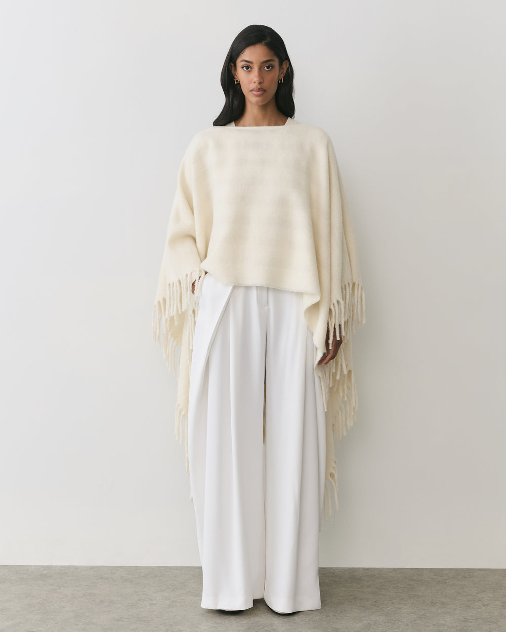 Person wearing a cape with fringe and wide-legged pants standing against a plain background.