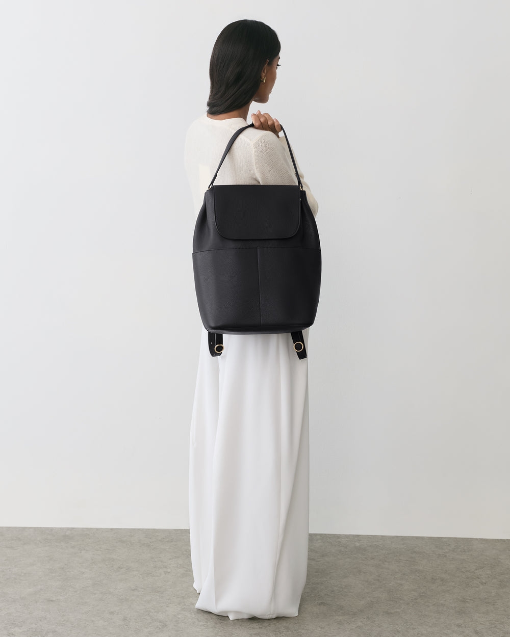 Person holding a large shoulder bag, wearing a long dress, standing on a plain floor.