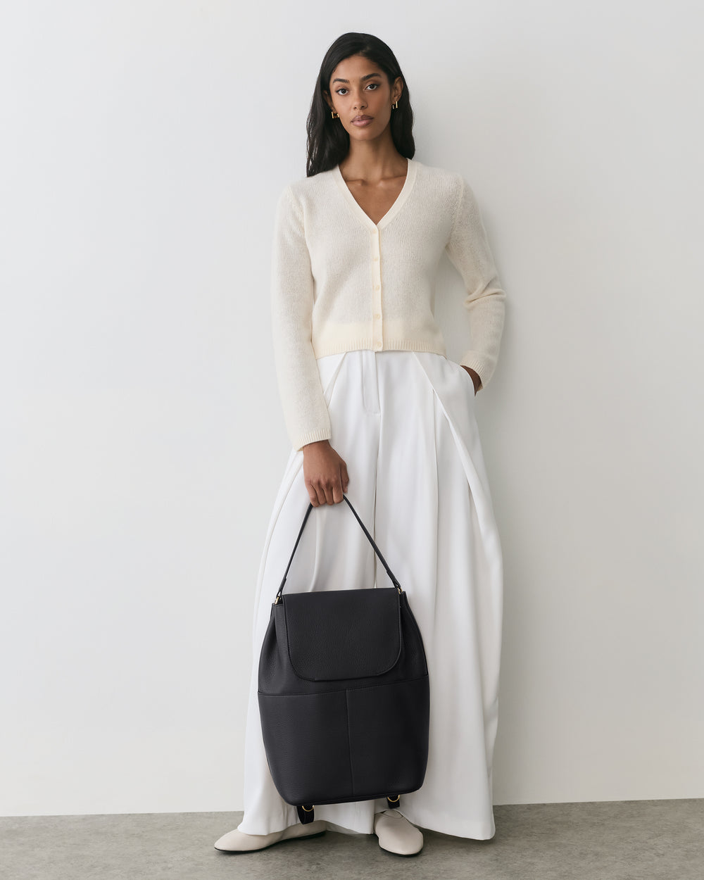 Person in cardigan and long skirt holding a large shoulder bag.