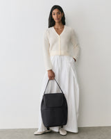 Person in cardigan and long skirt holding a large shoulder bag.